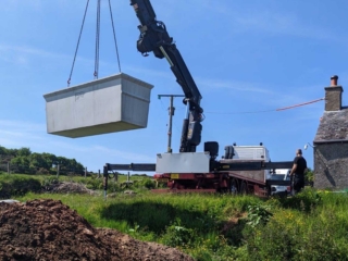 A septic tank being lifted by a crane in an installation